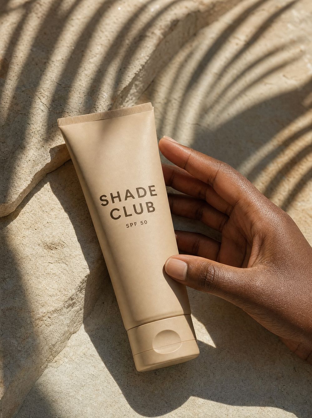 A Shade Club SPF 50 sunscreen tube held on sunlit stone