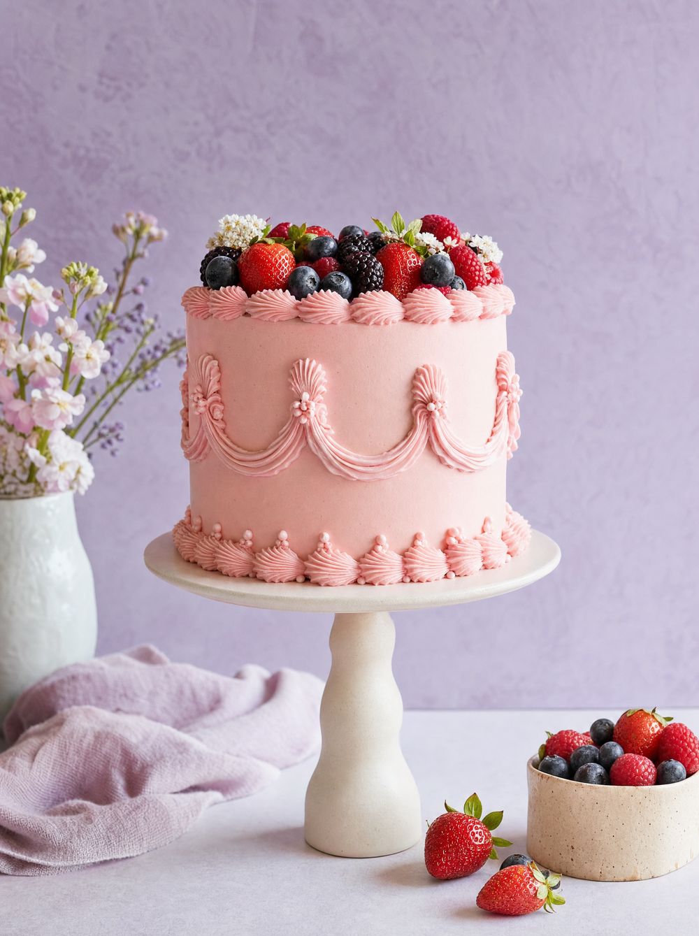 A pastel pink vintage-style birthday cake topped with berries